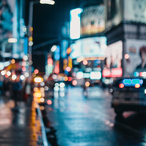 Visão embaçada de uma rua a noite, com luzes dos outdoors, carros e prédios.